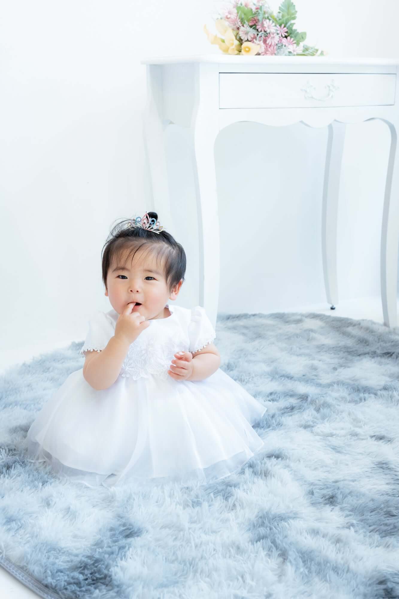 幼児の1歳祝いに白いドレスを着た女の子が座っているフォトスタジオのシーン