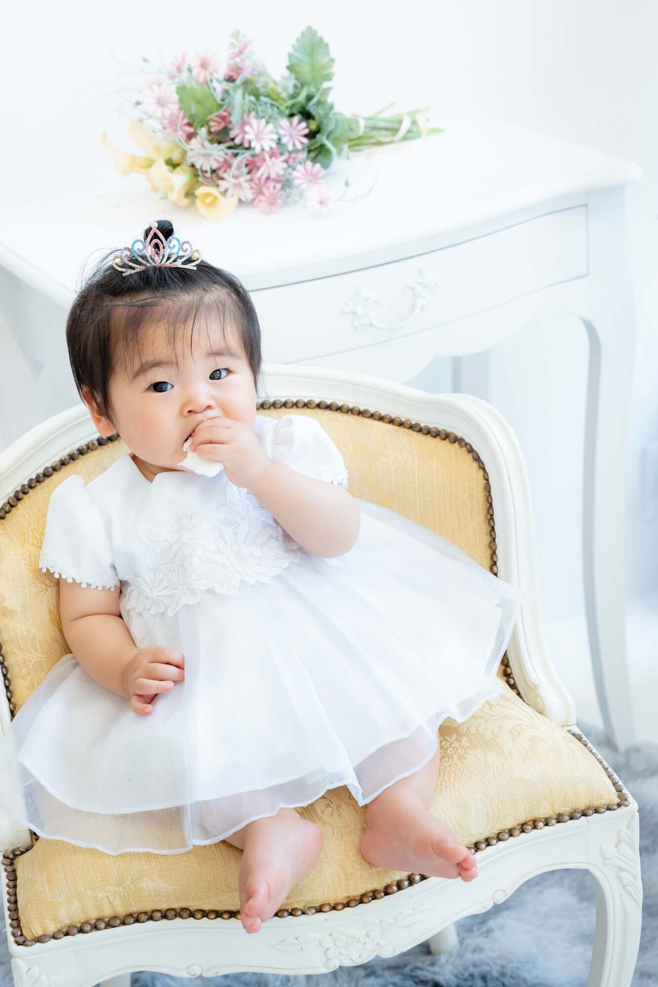 可愛い赤ちゃんがホワイトドレスを着て、王冠をかぶり椅子に座っている写真