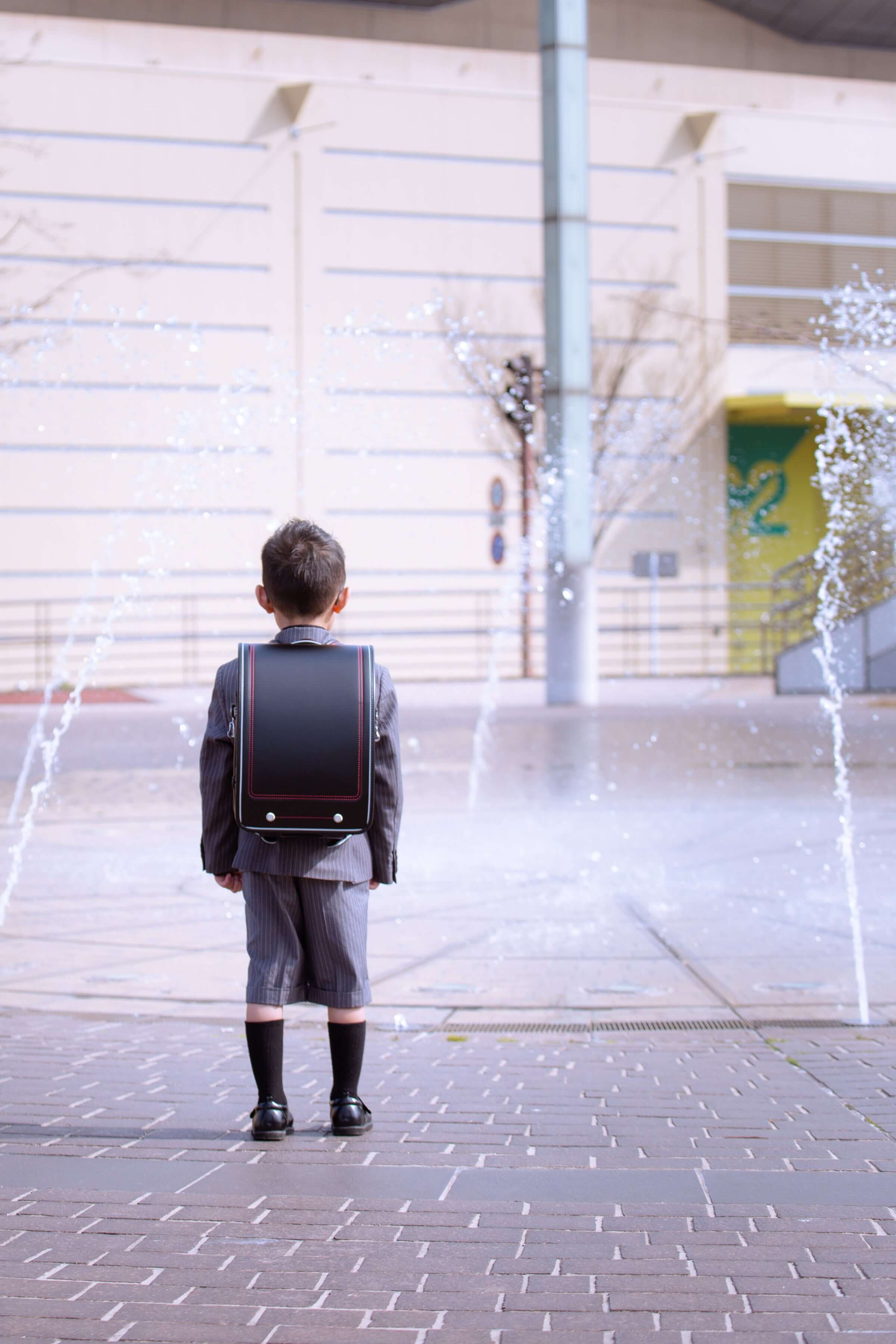 小学校入学の子どもがランドセルを背負い、噴水の前で待つ姿。フォトウエディング北九州の思い出作り。