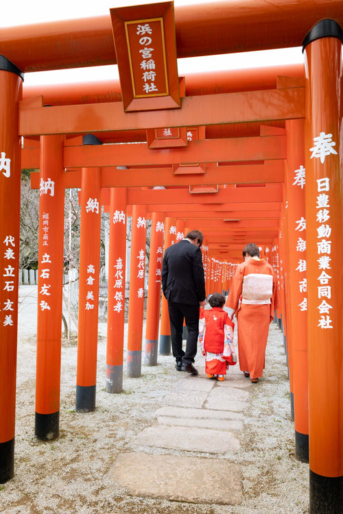 家族が神社の鳥居を歩く七五三の光景、フォトウエディング北九州で特別な瞬間を捉えた。