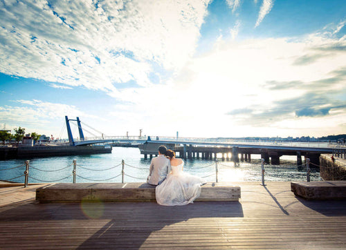 新郎新婦が北九州の海辺でロケション撮影を楽しむフォトウエディング。美しい夕焼けが背景。