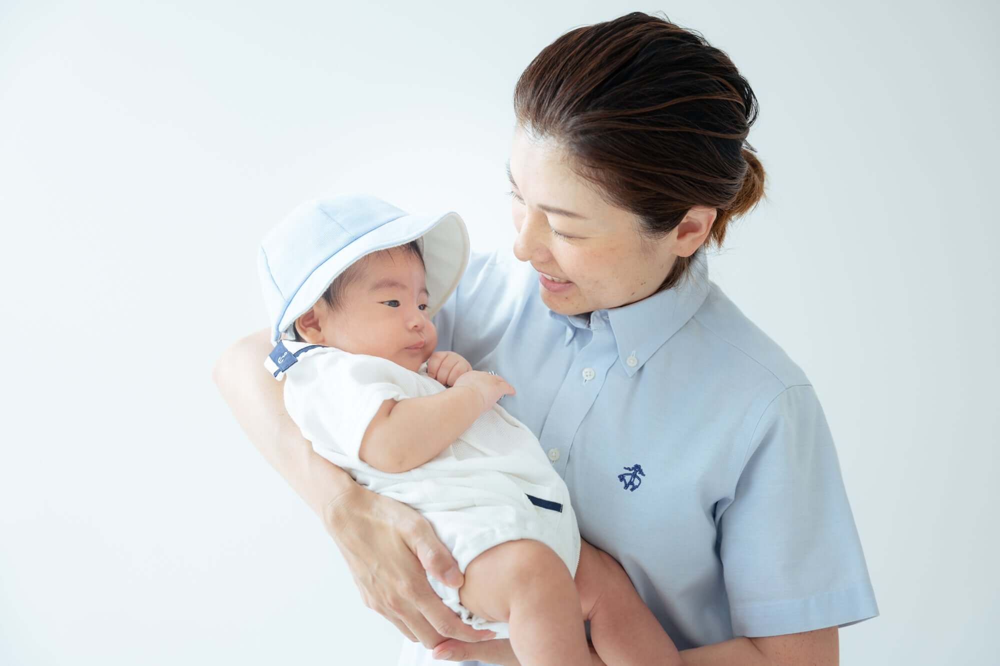 母親と赤ちゃんが親子コーデを楽しむシーン、シンプルな背景で幸せな瞬間を捉えた写真。