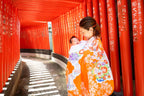 お宮参りの赤ちゃんを抱く母親、赤い鳥居背景にて、フォトウエディング北九州の魅力を表現