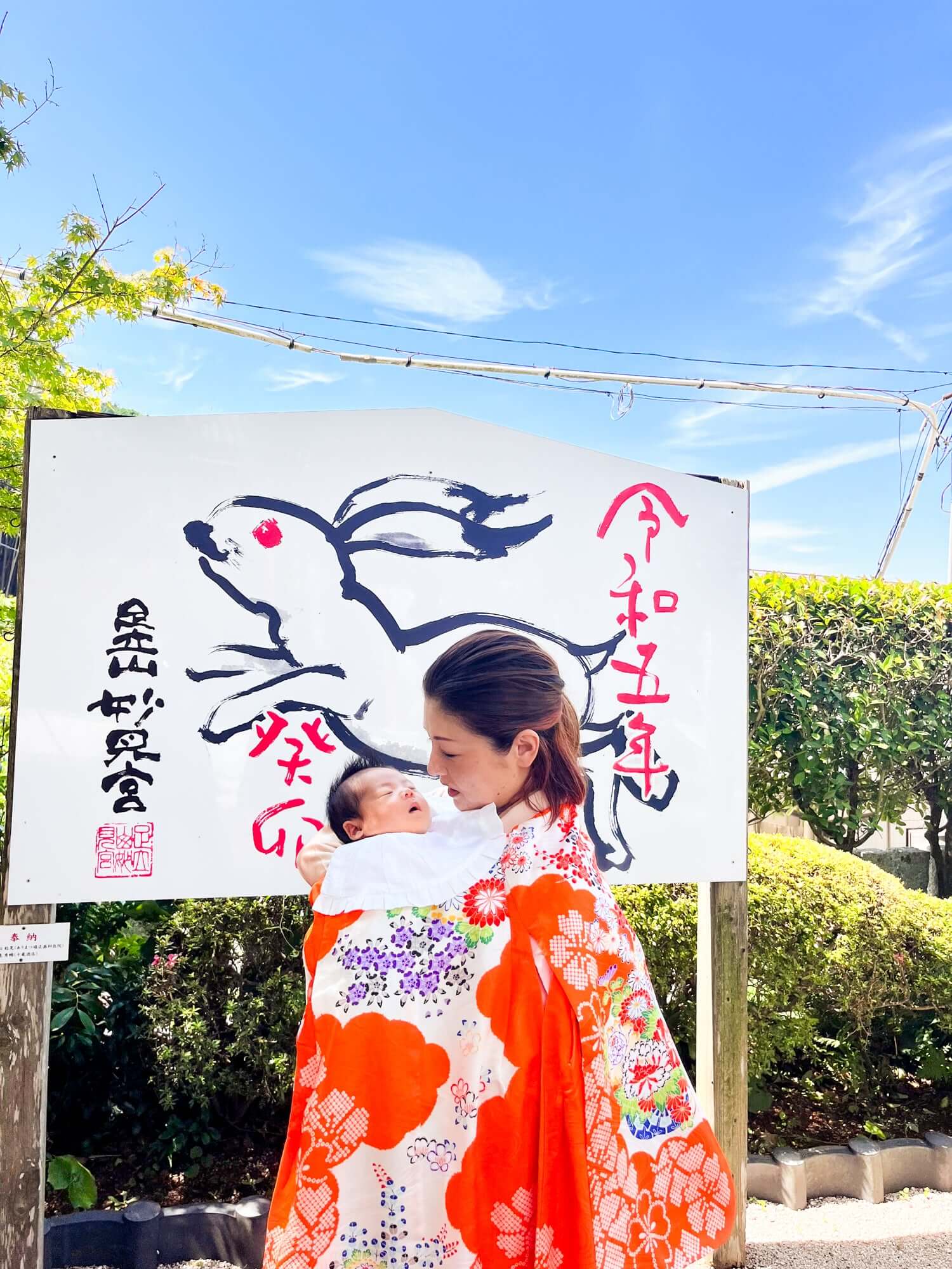 母親が赤ちゃんを抱き、伝統的な着物を着て神社の前でお宮参りの様子を撮影。フォトウエディング北九州。