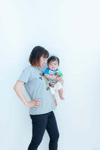 親子コーデの写真。母親が子供を抱えて立っているシンプルな背景での撮影。