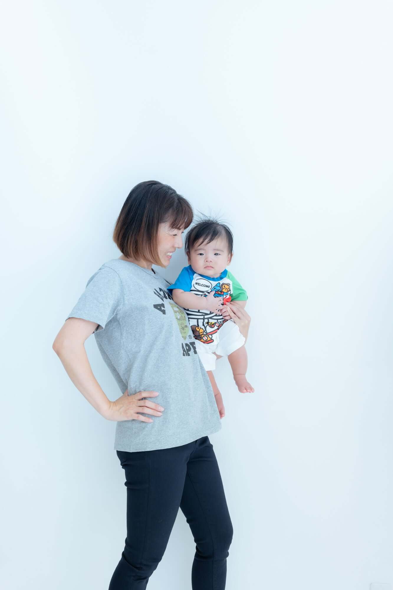 親子コーデの写真。母親が子供を抱えて立っているシンプルな背景での撮影。