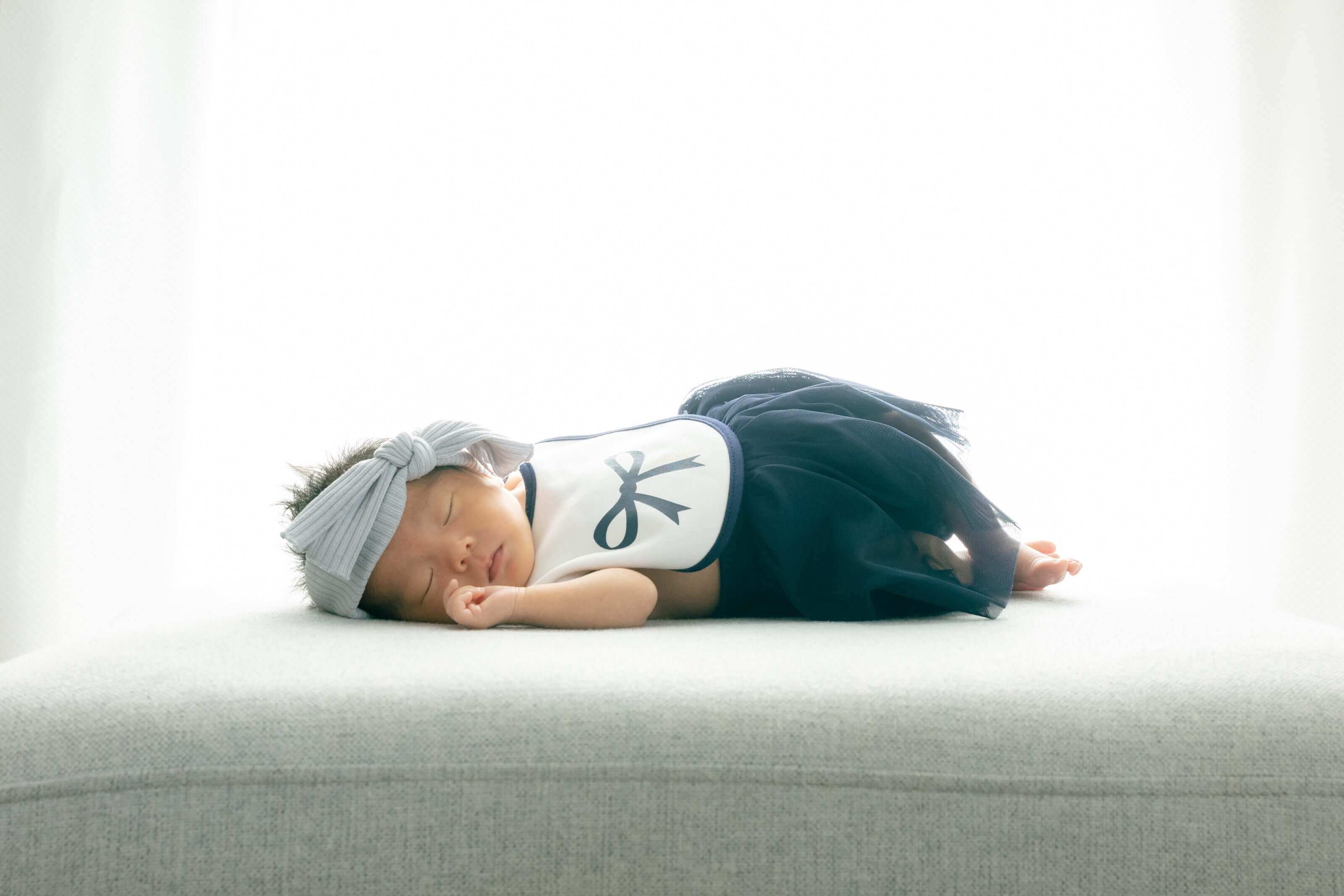 赤ちゃんがかわいいドレスを着て穏やかに寝ている様子。フォトウエディング北九州での百日祝いの一シーン。